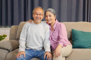 Evde kanepede oturan yaşlı çift kameraya gülümseyen ve evde dinlenen yaşlı çiftin portresi.