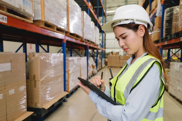 Warehouse manager in white helmet using tablet checking goods and supplies on shelves with goods background at warehouse factory, Logistic and business export concept