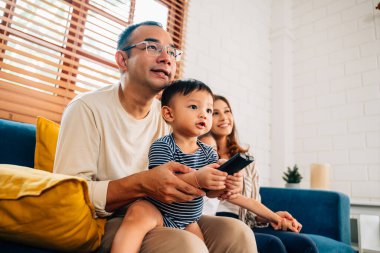 Mutlu bir aile oturma odasında birlikte televizyon izliyor, anne ve baba evde eğleniyor, aile oturma odasında rahat bir koltukta oturuyor, aile hayatı yaşıyor.