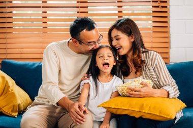 Mutlu bir aile oturma odasında film izliyor, anne ve baba evde aktivitelerle eğleniyor, aile patlamış mısır yiyor, oturma odasında rahat bir koltukta oturuyor, aile hayatı sürüyor.