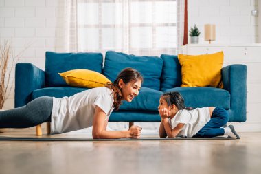 Genç anne ve kızı evde oturma odasında egzersiz yapıyor sağlıklı ve sağlıklı bir aile evde yoga egzersizi yapıyor evde birlikte oynuyorlar sağlıklı yaşam tarzına sahip bir aile.
