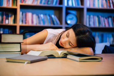 Eğitim için kütüphanede masada uzanan genç kadın, üniversite veya üniversite kampüsünde okuyan ve araştırma yapan insanlar, dil öğrenmek için kitaplıkta bulunan kitaplar