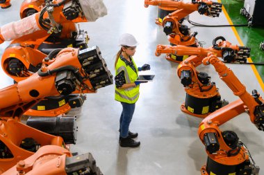 Endüstriyel fabrikada çalışan profesyonel kadın işyeri mühendisi, otomasyon teknolojisi fabrikasında robot makinesini kontrol eden kadın mühendis.