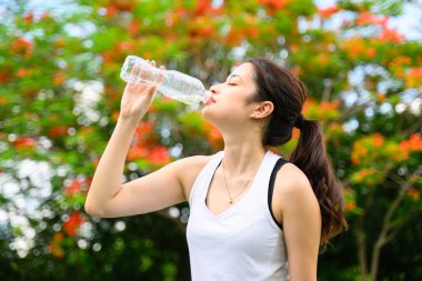 Sağlıklı genç bir kadın taze su içiyor ve yeşil parkta dinleniyor, kadın dışarıda mutlulukla yoga yapıyor, sabahları açık havada yoga yapan sağlıklı bir kadın.