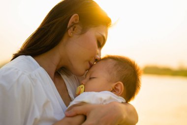 Sevgi dolu bir anne yeni doğan bebeğini parkın gün batımında kucağında taşır, mutlu bir aile hafta sonu parkta dinlenir ve eğlenir, neşeli bir anne ve bebek parkta pikniğin tadını çıkarırlar.