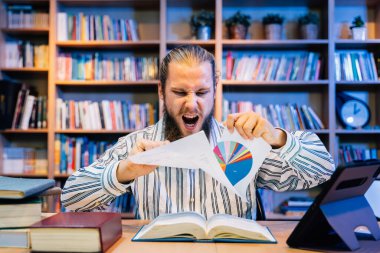 Kütüphane odasında okumaktan ve çalışmaktan yorgun düşmüş genç bir adam, uykucu bir üniversite öğrencisi, kütüphanede sıkı çalışan yorgun bir adam, kötü baş ağrısı, gözleri olan bir adam.