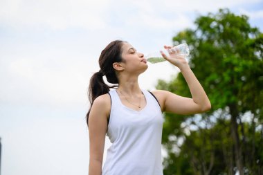 Sağlıklı genç bir kadın taze su içiyor ve yeşil parkta dinleniyor, kadın dışarıda mutlulukla yoga yapıyor, sabahları açık havada yoga yapan sağlıklı bir kadın.