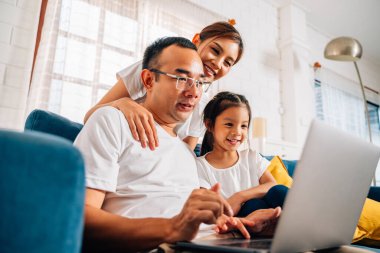 Aile babası anne ve kızı dizüstü bilgisayar kullanıyor ve oturma odasında internette sörf yapıyor, mutlu bir aile evde birlikte oynuyor, mutlu bir aile.