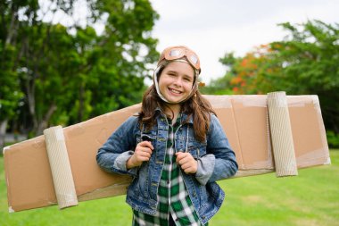 Mutlu kız hafta sonu bahçede kartondan oyuncak uçak el işi, yaratıcı aktiviteleri olan çocuk, yeşil alanda oyuncak uçak oynayan kız, uçmayı ve pilot olmayı hayal eden kız.