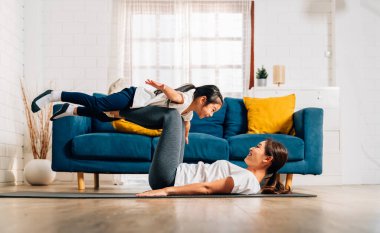 Genç anne ve kızı evde oturma odasında egzersiz yapıyor sağlıklı ve sağlıklı bir aile evde yoga egzersizi yapıyor evde birlikte oynuyorlar sağlıklı yaşam tarzına sahip bir aile.