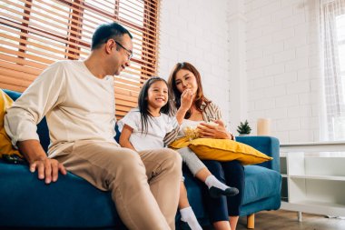 Mutlu bir aile oturma odasında film izliyor, anne ve baba evde aktivitelerle eğleniyor, aile patlamış mısır yiyor, oturma odasında rahat bir koltukta oturuyor, aile hayatı sürüyor.