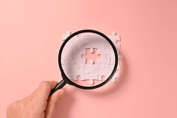 Hand holding magnifying glass with white square puzzle pieces grid of business background, Jigsaw on background, Mock up on background with copy space for text or symbols, Background with copy space