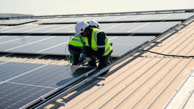 Güneş enerjisi tarlasında güvenlik kaskı olan profesyonel mühendisler, enerji fabrikasının çatısında güneş pili olan teknisyenler, sürdürülebilir kaynak kavramı