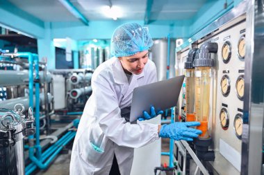 Şişeleme fabrikası işçisi sevkiyattan önce su şişelerinin kalitesini kontrol ediyor. Bitkide kullanılan ters osmoz sistemi. Su saflığı ve şişeleme sürecinde kalite kontrolü. Yüksek kalite fotoğraf.