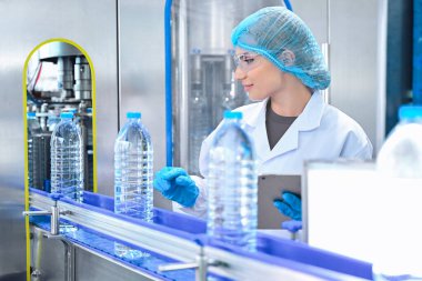 Şişeleme fabrikası işçisi sevkiyattan önce su şişelerinin kalitesini kontrol ediyor. Bitkide kullanılan ters osmoz sistemi. Su saflığı ve şişeleme sürecinde kalite kontrolü. Yüksek kalite fotoğraf.