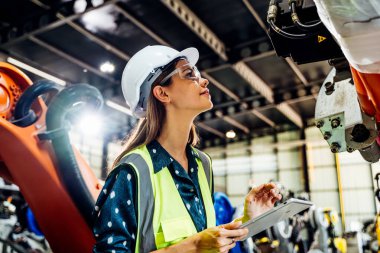 Endüstriyel fabrikada çalışan profesyonel kadın işyeri mühendisi, otomasyon teknolojisi fabrikasında robot makinesini kontrol eden kadın mühendis.
