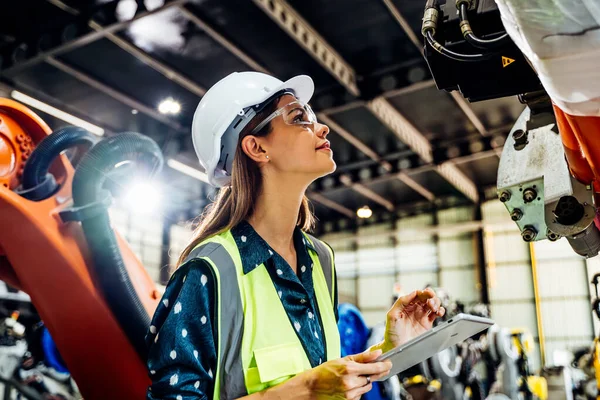 Endüstriyel fabrikada çalışan profesyonel kadın işyeri mühendisi, otomasyon teknolojisi fabrikasında robot makinesini kontrol eden kadın mühendis.
