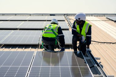 Güneş enerjisi tarlasında güvenlik kaskı olan profesyonel mühendisler, enerji fabrikasının çatısında güneş pili olan teknisyenler, sürdürülebilir kaynak kavramı