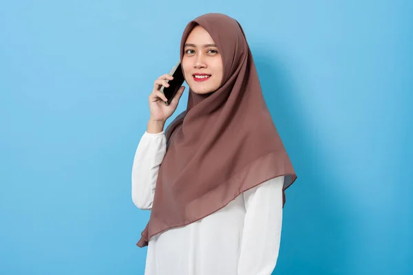 Portrait of Happy smiling muslim woman using mobile phone isolated on blue background