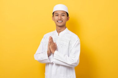 Yakışıklı Asyalı Müslüman adam, ramazan boyunca turuncu arka planda izole bir şekilde selam veriyor. Ramazan ve bayramın kutlu olsun..