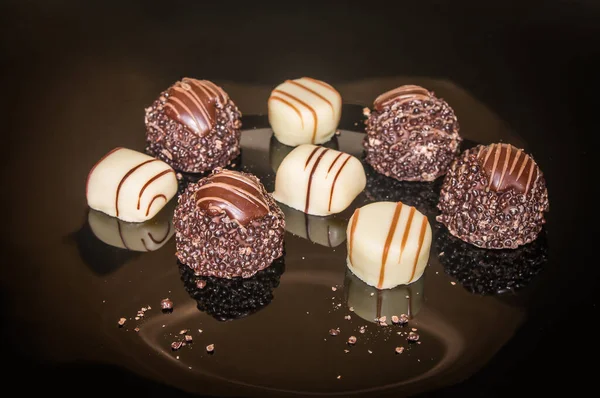 Luxurious sweets chocolate truffles. Pralines designed in Belgium and arranged on the table. Candies on a black background. Assortment sweet confectionery of dark, white and milk chocolate with nuts.