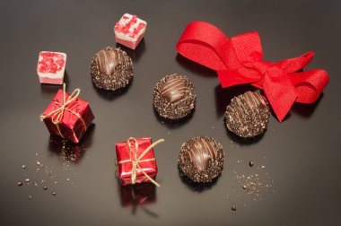 Chocolate pralines truffles and red ribbon tied into bow and two small props Christmas square box gift. Decoration for Christmas day. Festive decoration.