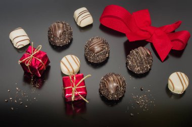 Chocolate pralines truffles and red ribbon tied into bow and two small props Christmas square box gift. Decoration for Christmas day. Festive decoration.