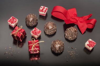 Chocolate pralines truffles and red ribbon tied into bow and two small props Christmas square box gift. Decoration for Christmas day. Festive decoration.