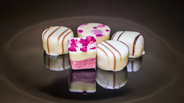 5 pieces of white chocolate on the dark background. Luxurious colorful handmade chocolate praline. Variety of strawberry, coconut, vanilla and lemon truffles.
