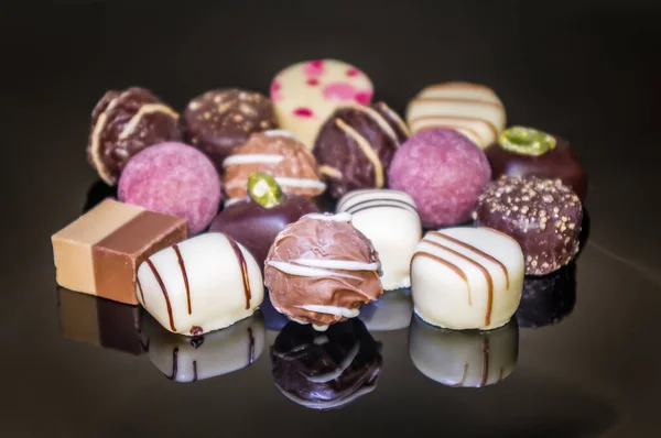Luxurious mixed colorful handmade chocolate praline. Variety of strawberry, coconut, vanilla and lemon truffles. Pralines designed in Belgium and arranged on dark background. Variation Of Chocolate Candies.