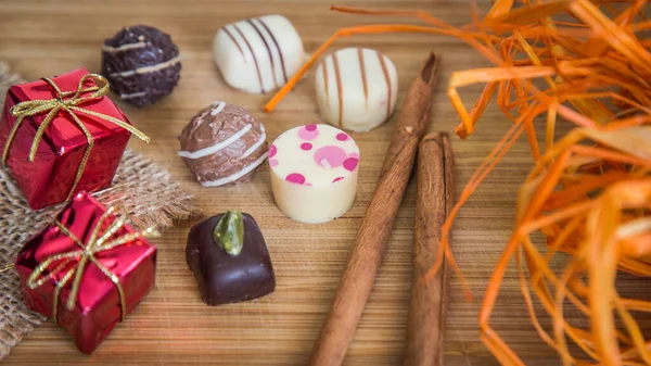 stock image Chocolate pralines with pink dots. Small red packages and orange decoration, with cinnamon stick.