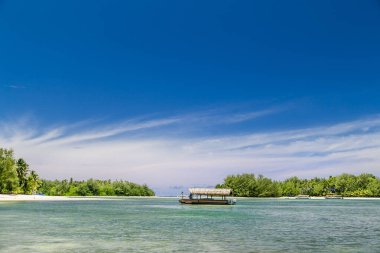 Tropik körfez, Cook Adaları 'ndaki cennet istikameti. Güneşli bir günde Rarotonga Sahili. Denizde bir tekne. Bulutlu mavi gökyüzü. Parçalı bulutlu. Uzakta palmiye ağaçları.