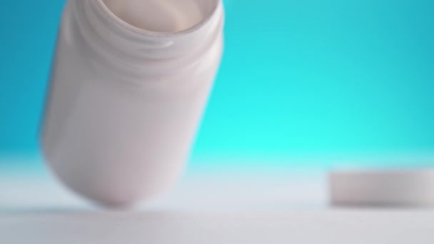 鎮痛剤のボトルテーブルの上にトッピング 青色の背景にスローモーションでこぼれるホワイトパラセタモール錠 — ストック動画