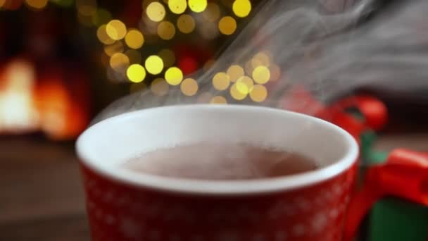 Kırmızı Kupada Sıcak Buharlı Çay Arkaplanda Bulanık Şömine Noel Işıkları — Stok video