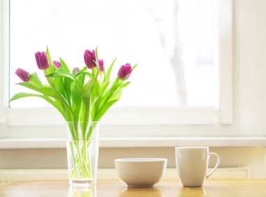 Cozy breakfast with a cup of hot tea or coffee and a bowl of muesli with a magenta tulips bouquet on the wooden table in the front of a window. Good morning. Copy space. High quality photo.