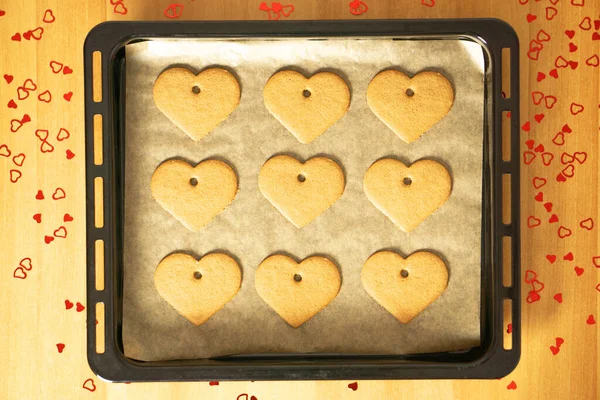 Romantic heart cookies on a baking tray on the table with many red hearts decorations. Valentines day concept. High quality photo.