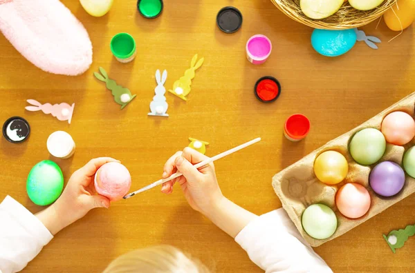 Child hands painting colored eggs for Easter on the wooden table at home. Happy Easter. Preparation for Easter. High quality photo.