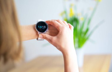 Arka planda bir buketle beyaz akıllı saat takan bir kadının eli. Teknoloji ve insan konsepti. Modern yaşam tarzı. Bir kadın şık akıllı saati kontrol ediyor..