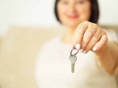 Çekici, orta yaşlı bir kadının elinde yeni evinin anahtarını tutarken. İnsanlar, gayrimenkul ve mülk kavramı. 