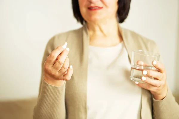 stock image Retired woman in casual clothes at home holding pill and glass water. Healthy middle aged 60s woman holding glass of water and her medication. Happy adult woman taking vitamin pill.