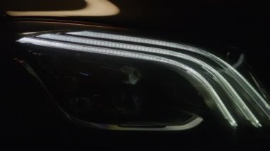 Close up view on details of headlights from unrecognizable prestigious black luxury modern car. Car light lights up with white successively, starting the engine. Shot in high quality 4K. Head light