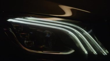 Prestijli siyah lüks modern arabanın farları aydınlanıyor, detaylara yakından bakılıyor, tanınamaz hale geliyor. Işıklar arka arkaya beyazla yanıyor, motoru çalıştırıyor. Yüksek kalite 4K ile vurulmuş.