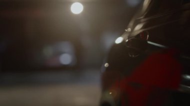 Tanımlanamayan bir kadının siyah arabaya yaklaşıp gece park yerinde kapısını açması. Kadın eli araba sapına dokunuyor, kırmızı ışık yüzeylere yansıyor, karanlık yeraltı otoparkı, 4K görüntü.