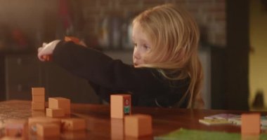 Child responds someone emotionally while playing by the table with orange wooden toy blocks, autistic child, cute kid builds street with houses. Mental disorder, domestic background. HQ 4K footage