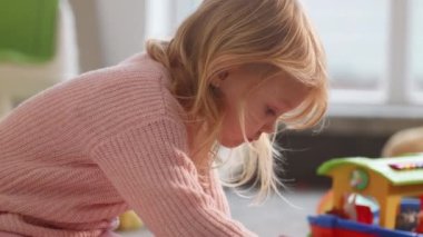 Sevimli sarışın kız yerde tek başına oynamakla meşgul, otistik çocuk takım aktivitelerinden kaçınıyor. Düşünceli bir çocuk, parlak bir hemşirelik geçmişi, doğal gün ışığı. Akıl sağlığı hastalıkları. Karargah 4k görüntüsü