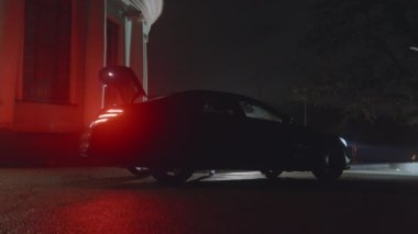 Gece açık hava sahnesi, bir arabanın bagajı otomatik olarak açılıyor, bir kadın gelip parlak bir elbise alıyor, kırmızı araba ışıkları. Siyah kravat etkinliği, konser ya da gece gösterisi için hazırlanıyorum. Ağır çekim Karargah 4K görüntüsü