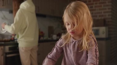 Anne ve kızı evde birlikte meşguller. Oyuncak blokları masaya kuruyorlar. Mutfakta yemek pişiriyorlar. Parlak ahşap tuğlalar, rahat ev içi, gerçek hayat görüşü, ağır çekim HQ 4k görüntü.