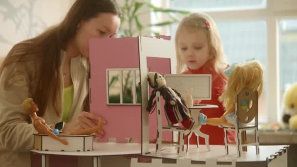 木製のおもちゃの家を組み立てる過程で母と娘は 人形で遊んで 家族の遊びの喜び 明るい居心地の良い家で日当たりの良い週末のための適切な詳細を探しています 本部4K映像 — ストック動画