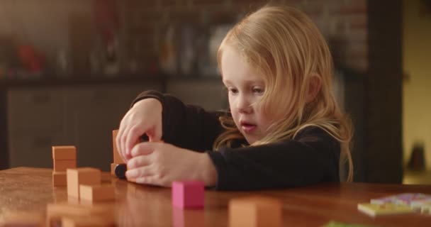 かわいい赤ちゃんの女の子が行うテーブルの上で忙しいゲーム オレンジの木製のおもちゃのブロック 恥ずかしがり屋の自閉症の子供だけで再生され 家と通りを構築します 精神障害 国内の背景 高品質4K映像 — ストック動画