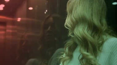 Modern saydam cam asansörde bir bayan aşağı iniyor. Sarışın kadın yüzünü gizliyor, cam yüzeyine yansıyan bir portre. Gökdelen ya da otel. Asansör aşağı iniyor. Yüksek kalite 4k görüntü